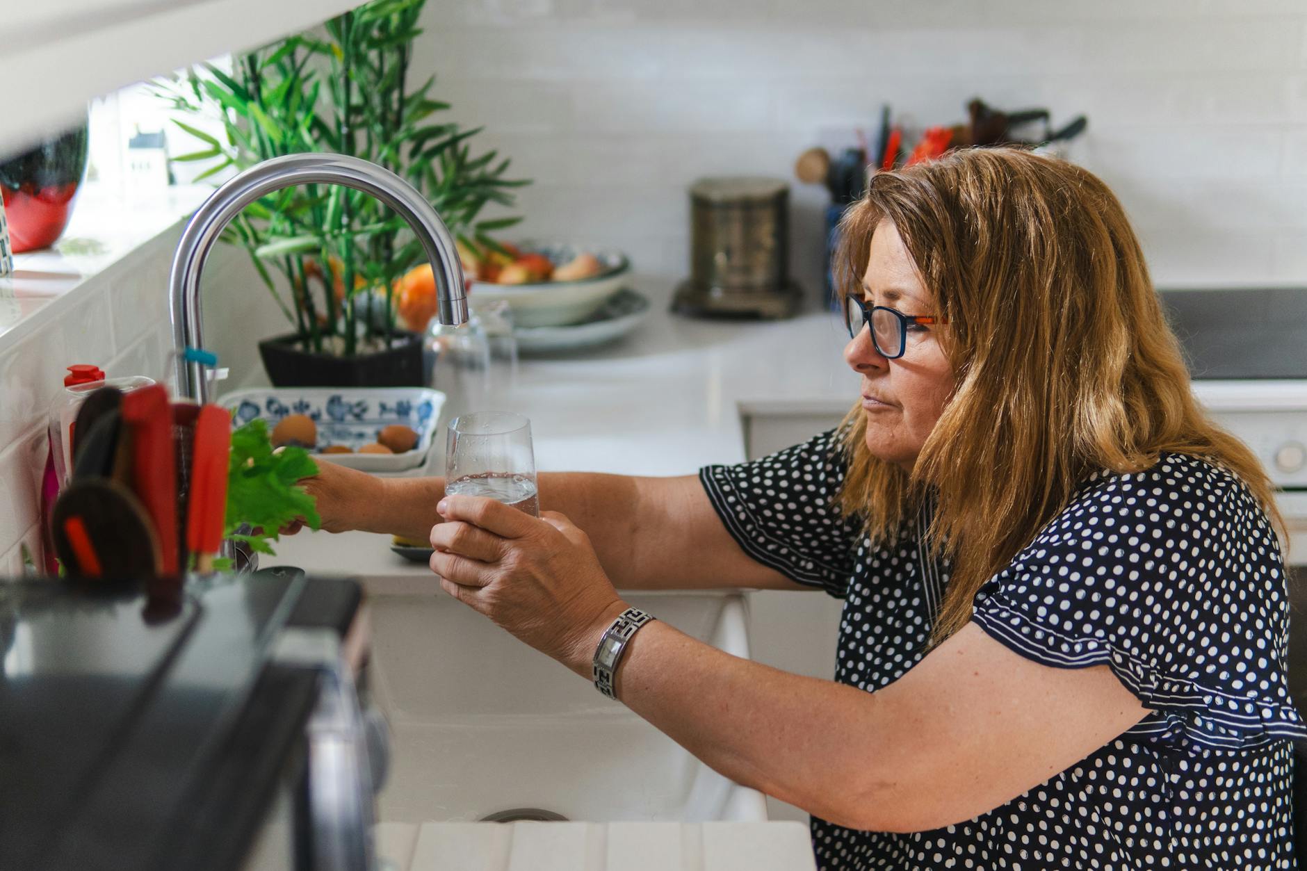 A woman inspecting a kitchen tap in a modern Dubai home to reduce household water use