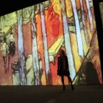 A woman walks through a glowing digital projection room at an immersive art experience inside a Dubai mall